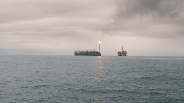 FPSO tanker vessel near Oil Rig platform. Offshore oil and gas industry. Flare is burning with smoke. Environmental pollution