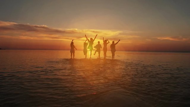 Friendship Freedom Beach Summer Holiday Concept. Beauty and joyful teenager friends having fun, dancing, spraying over summer sunset. Beach party. Sun flare. Slow motion
