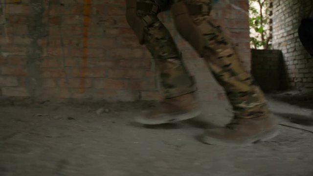 Close-up of army soldiers legs in old combat boots running into dusty building during military operation. Side view. Elite squad of marines in uniform invading the building captured by terrorists.