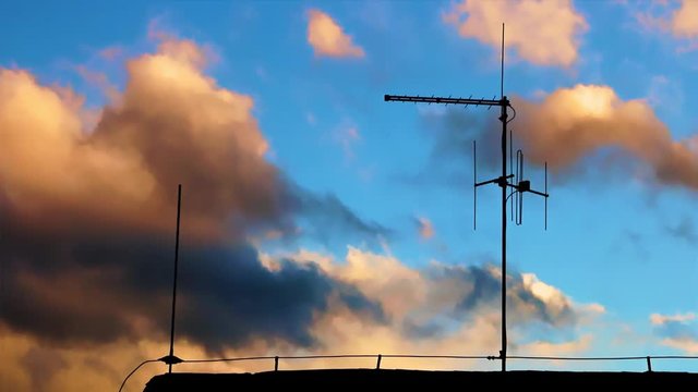 An antenna silhouette on an evening sky with fast-moving clouds. Sunset over the roof with an antenna.