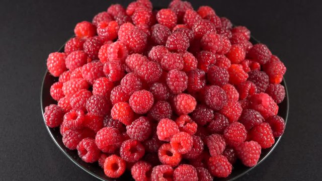 Fresh, ripe, juicy raspberry background, close up berry, rotation loopable 4k . Food  background. Gastronomy concept, organic food. Macro red raspberries fruit in plate on black background