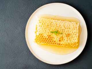 one plate with honey in honeycomb, close-up, on brown ceramic plate, on gray stone table, top view, flat lay