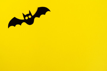 Holiday decorations for Halloween. Black paper bat on a yellow background, top view.