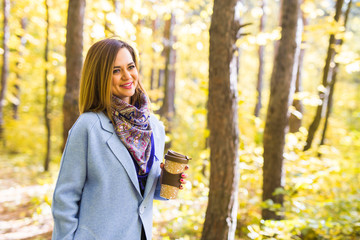 Attractive woman holding a cup of takeaway coffee cup on autumn street