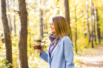 Attractive woman holding a cup of takeaway coffee cup on autumn street