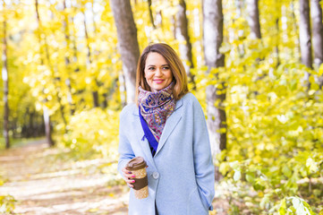 Attractive woman holding a cup of takeaway coffee cup on autumn street