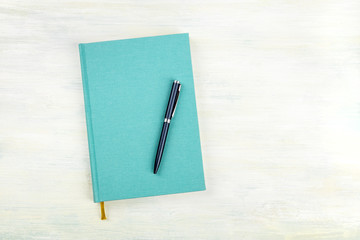 An overhead photo of a teal blue journal with a pen, an elegant notebook or planner with a place for text