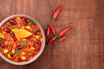 Chili con carne, traditional Mexican dish, shot from the top on a dark wooden background with chilli peppers and copy space