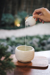 One hand pouring milk in the Matcha green tea bowl