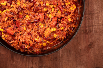 A closeup photo of a large cast iron pan with chili con carne, shot from above on a dark rustic wooden background with copy space