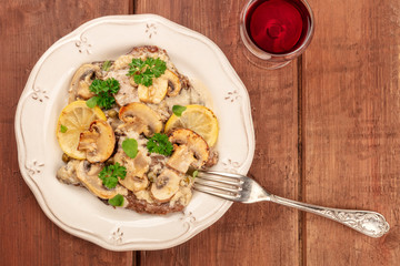 Scallopine di vitello, veal scallopini, with a mushroom sauce, lemons, and parsley, shot from above on a dark wooden texture with red wine and copy space