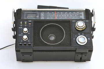 Old black multiband radio receiver with an external transverse antenna on the top panel, with two protruding chrome handles on the front panel, the speaker looks through the metal grille