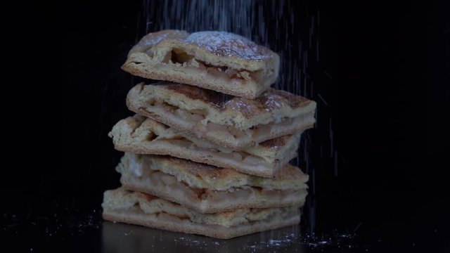 Apple pie sprinkled with powdered sugar on a black background, close up. Apple pie with cinnamon, slow motion