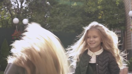 Two pretty fair-haired girls toss their hair, play peek-a-boo, and adjust hair in the wind. The older girl stands back to the camera and tidies hair of the younger girl.