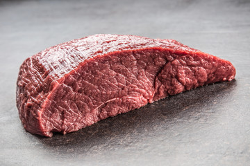 Portion of raw beef thigh on dark butcher board