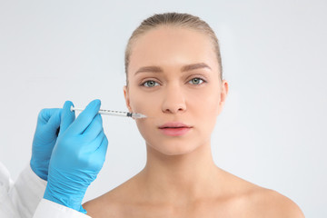 Young woman getting facial injection on white background. Cosmetic surgery concept