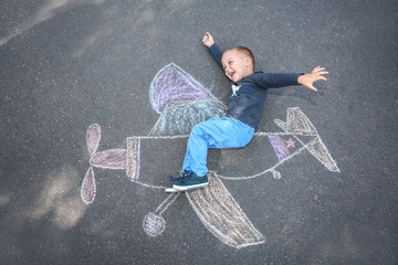 Little child lying near chalk drawing of airplane on asphalt, top view - Powered by Adobe