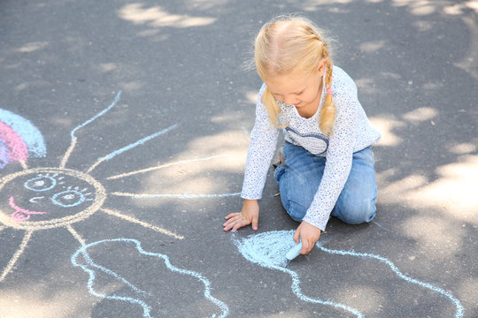 Little child drawing with colorful chalk on asphalt