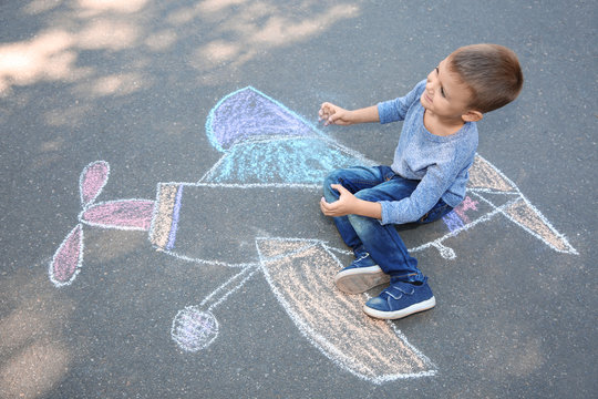 Little child sitting near chalk drawing of airplane on asphalt