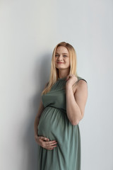 Fototapeta premium Young pregnant woman touching belly on light background