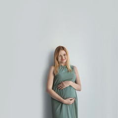 Obraz premium Young pregnant woman touching belly on light background