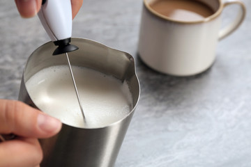 Woman using milk frother in pitcher on table, closeup