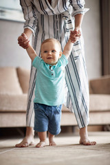 Smiling baby boy making first steps with mother.