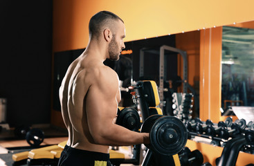 Fototapeta na wymiar Strong young man lifting dumbbells in gym