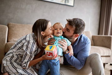 family, parenthood and people concept - happy mother and father kissing little baby at home.