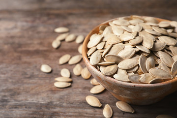 Full bowl of raw pumpkin seeds on wooden background