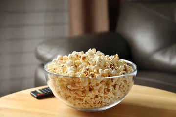 Tuinposter Bowl of popcorn and TV remote on table against blurred background. Watching cinema © New Africa