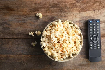  Bowl of popcorn and TV remote on wooden background, top view with space for text. Watching cinema © New Africa