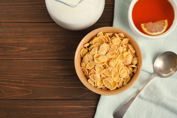 Flat lay composition with healthy cornflakes in bowl on wooden table. Space for text