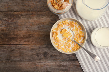Flat lay composition with healthy cornflakes and milk in bowl on wooden table. Space for text