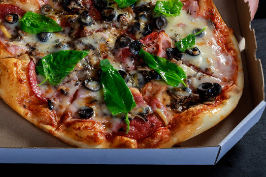 Delicious fresh baked pizza in cardboard box.Tasty fast food dish served in brown paper package.Tomato sauce,black olives,feta cheese and green leaves for good taste