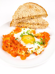Fried egg, sunny side up, with chopped tomato and toast on the side of place