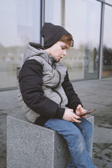 7 year old boy playing with smartphone, sitting outside in winter jacket and knit hat
