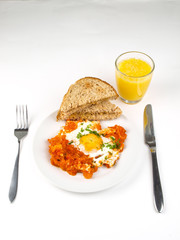 Fired egg, with chopped tomato, and toast on the side of plate, with juice in glass on table