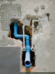 Detail of metal water pipes and PVC drain pipe blue color appear in smashed bathroom wall,Under-construction condominium site.