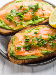 Rye bread avocado toasts with smoked salmon on white wooden board