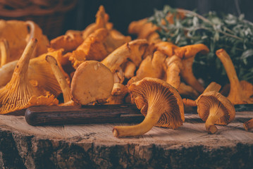 Wicker tray with chanterelle mushrooms on wooden table. Knife, basket with mushrooms and fresh herbs
