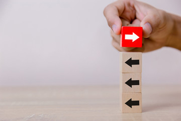 Hand putting wood cube block on top vertical red wooden blocks with white arrows facing opposite to...