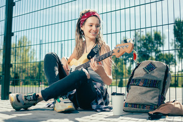 Happy lady smiling and enjoying playing the guitar outdoors