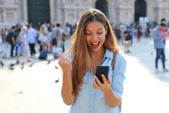 Excited young woman receiving good news on line in a smart phone outside on the street