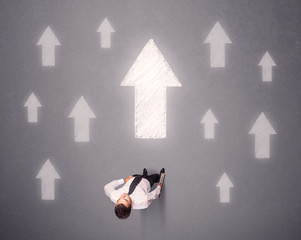 Young contemplating businessman stands in front of white arrows