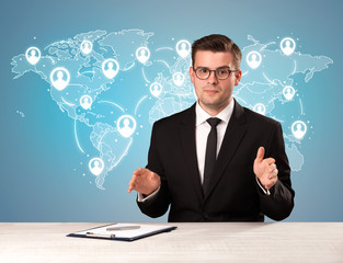 Young handsome businessman sitting at a desk with a blue world map behind him