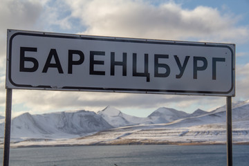 A road sign announcing entry into Barentsburg, written in Russian cyrillic letters, with snow-capped mountains and Isfjord fjord behind, on  Spitsbergen, Svalbard, Norway.