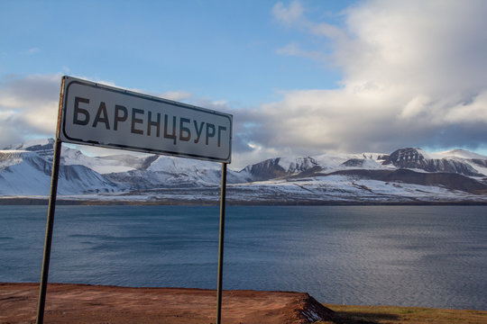 A road sign announcing entry into Barentsburg, written in Russian cyrillic letters, with snow-capped mountains and Isfjord fjord behind, on  Spitsbergen, Svalbard, Norway.