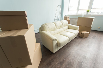 Relocation, moving and real estate concept- a new white sofa in empty room between an amount of boxes