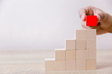 Hand arranging red wood block stacking as step stair,With the concept of a thriving business going for success.